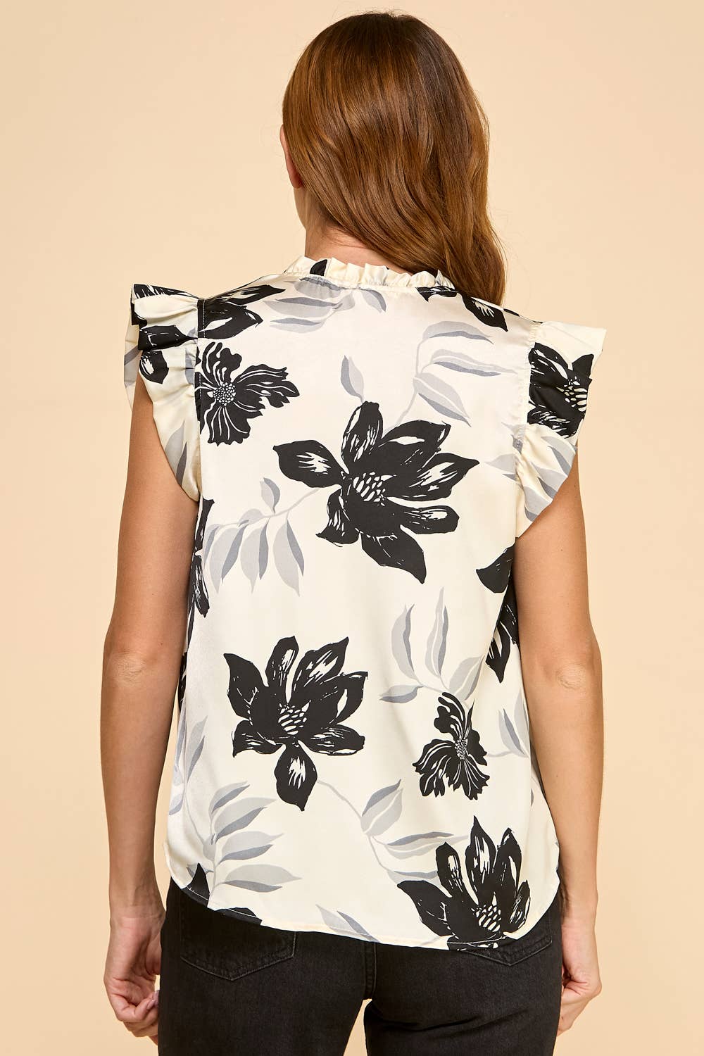 Woman wearing a sleeveless top with black floral patterns on a beige background