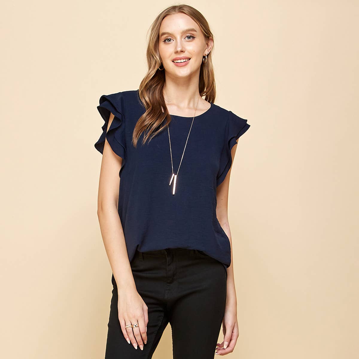 Woman wearing a navy blue top with ruffled sleeves on a beige background