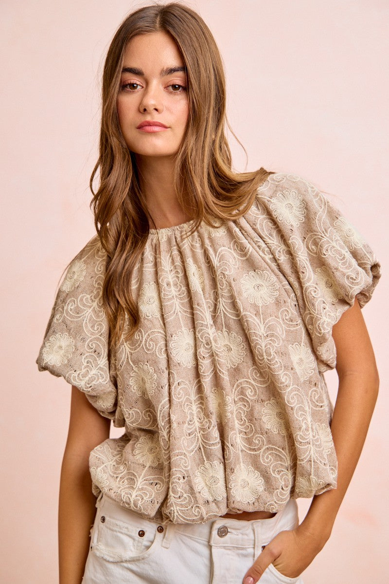 Woman wearing a beige lace blouse against a pink background
