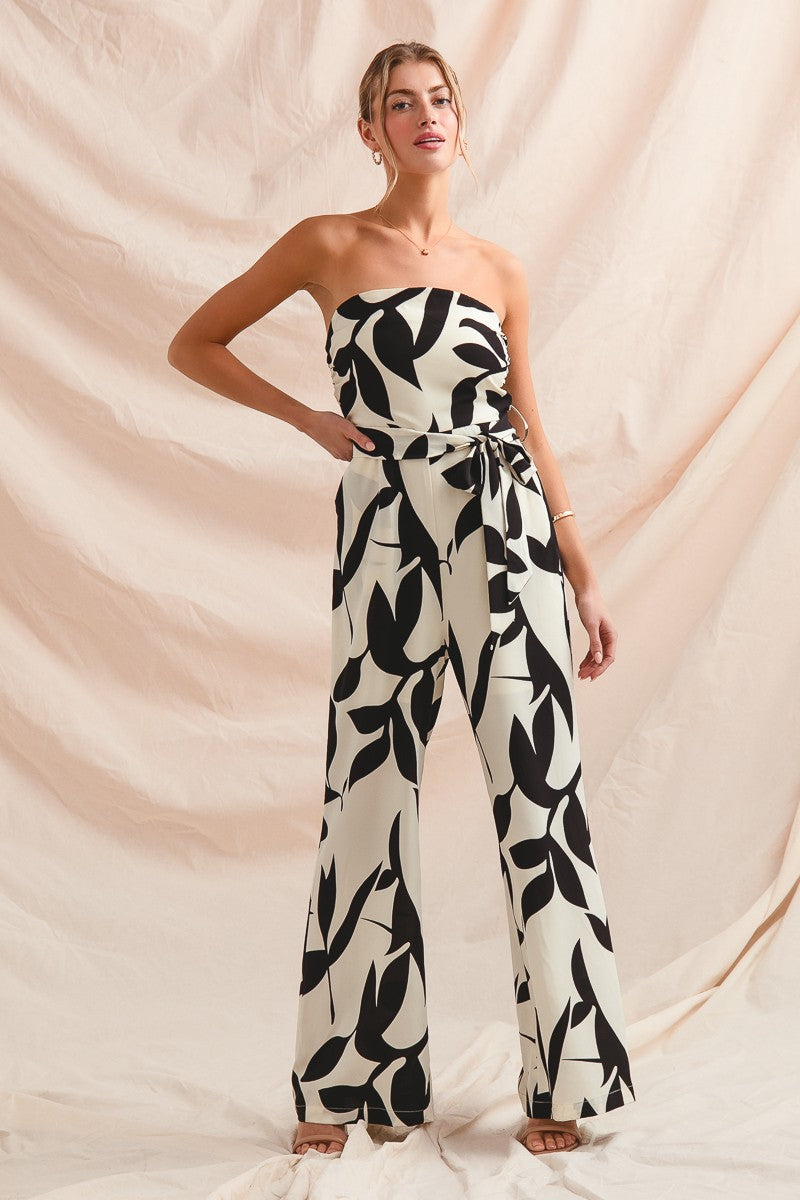 Woman wearing a strapless black and white leaf-patterned jumpsuit against a beige background
