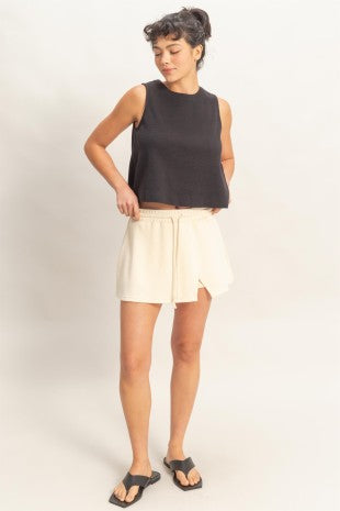Woman wearing a black sleeveless top and white shorts on a plain background