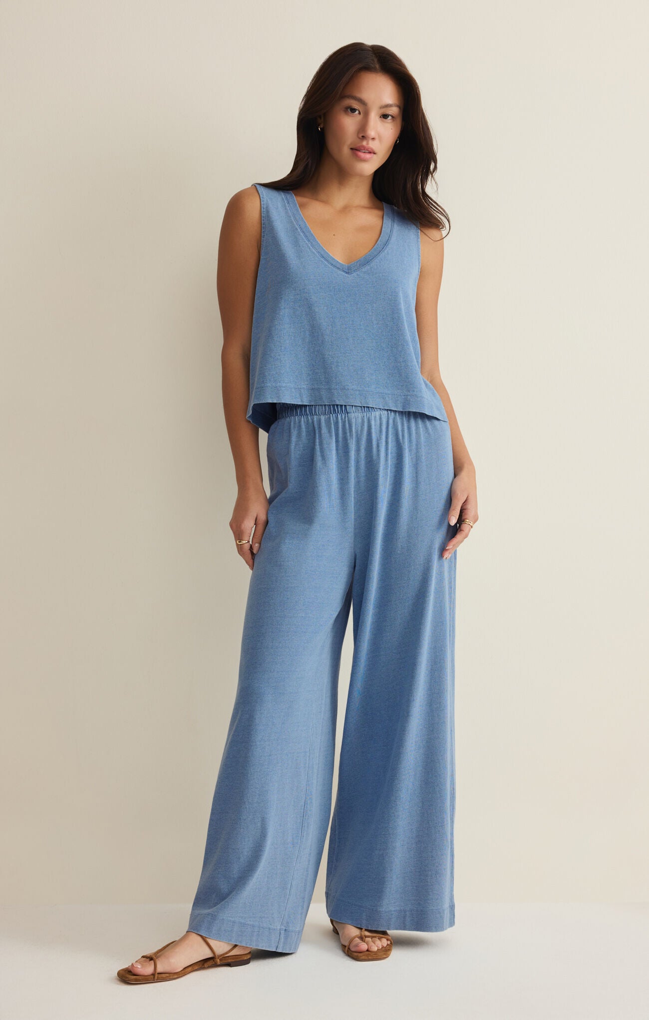 Woman wearing a blue sleeveless top and wide-leg pants on a beige background
