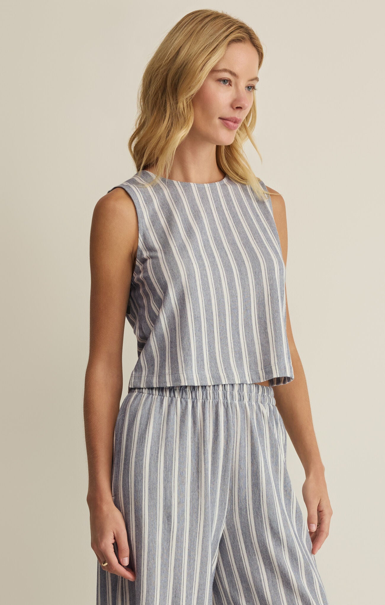 Woman wearing a sleeveless striped top and wide-leg pants against a beige background