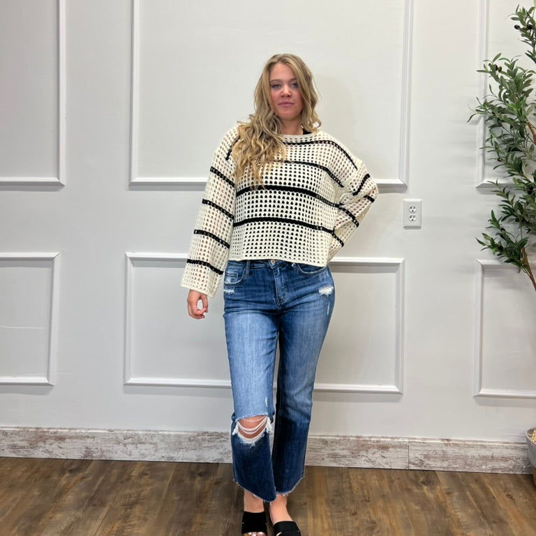Woman wearing a striped sweater and jeans standing in front of a white paneled wall.
