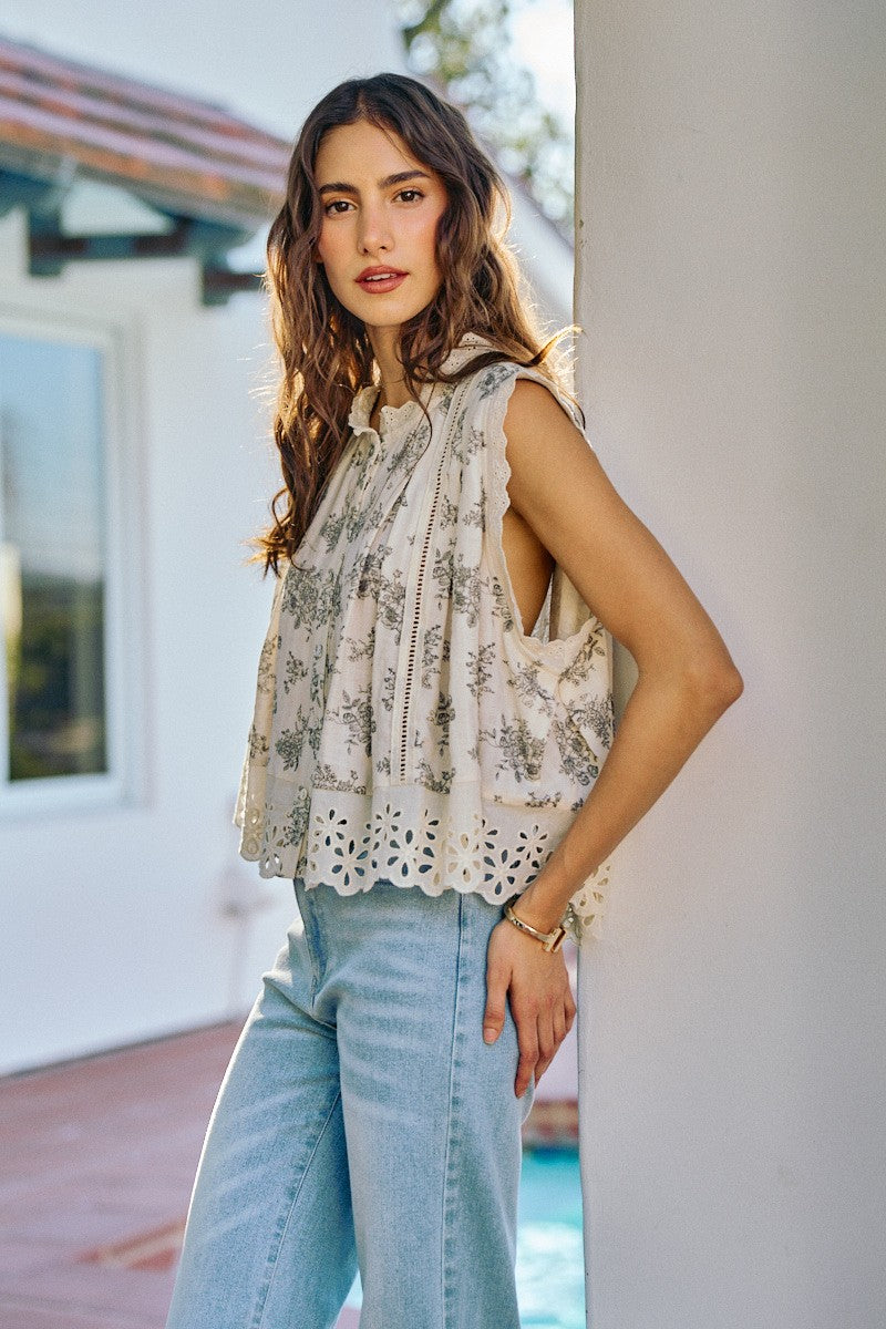 Woman wearing a sleeveless floral top and light blue jeans standing outdoors.