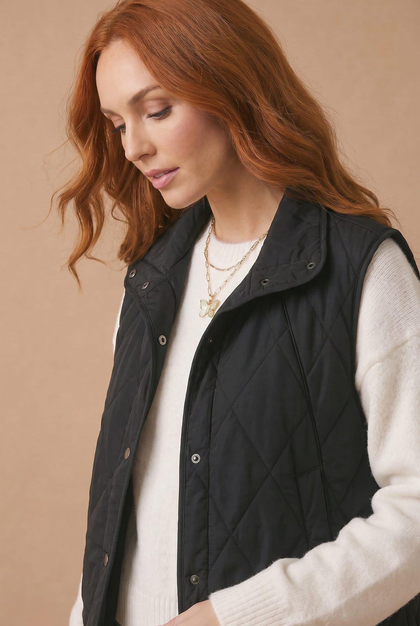 Woman wearing a black quilted vest over a white sweater on a beige background