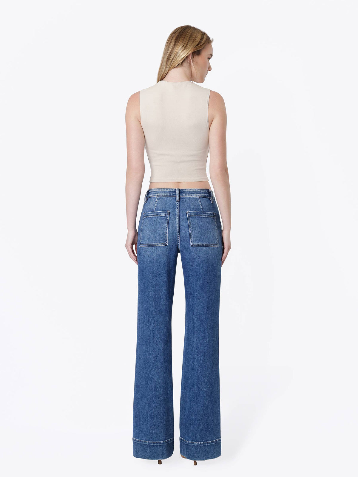A woman shown from the back wearing a beige ribbed sleeveless crop top and high-waisted, wide-leg blue denim jeans against a plain white studio background.