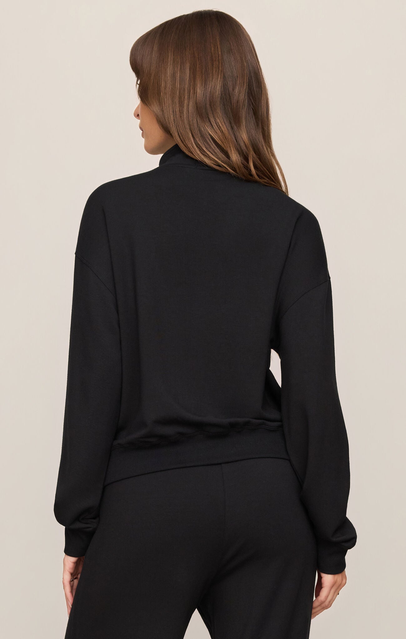 Woman wearing a black long-sleeve top and pants on a beige background