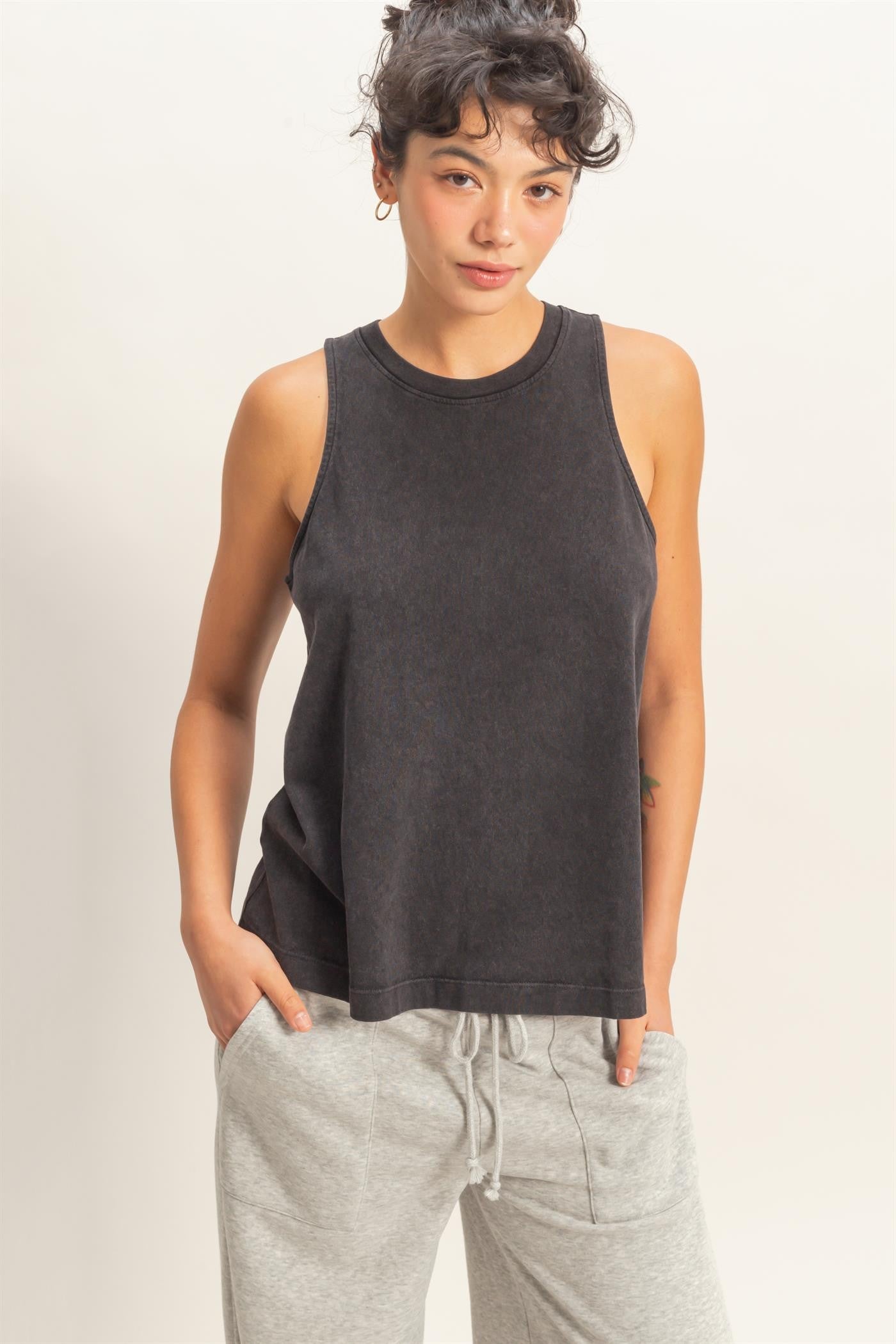 Woman wearing a black sleeveless top and gray sweatpants against a neutral background