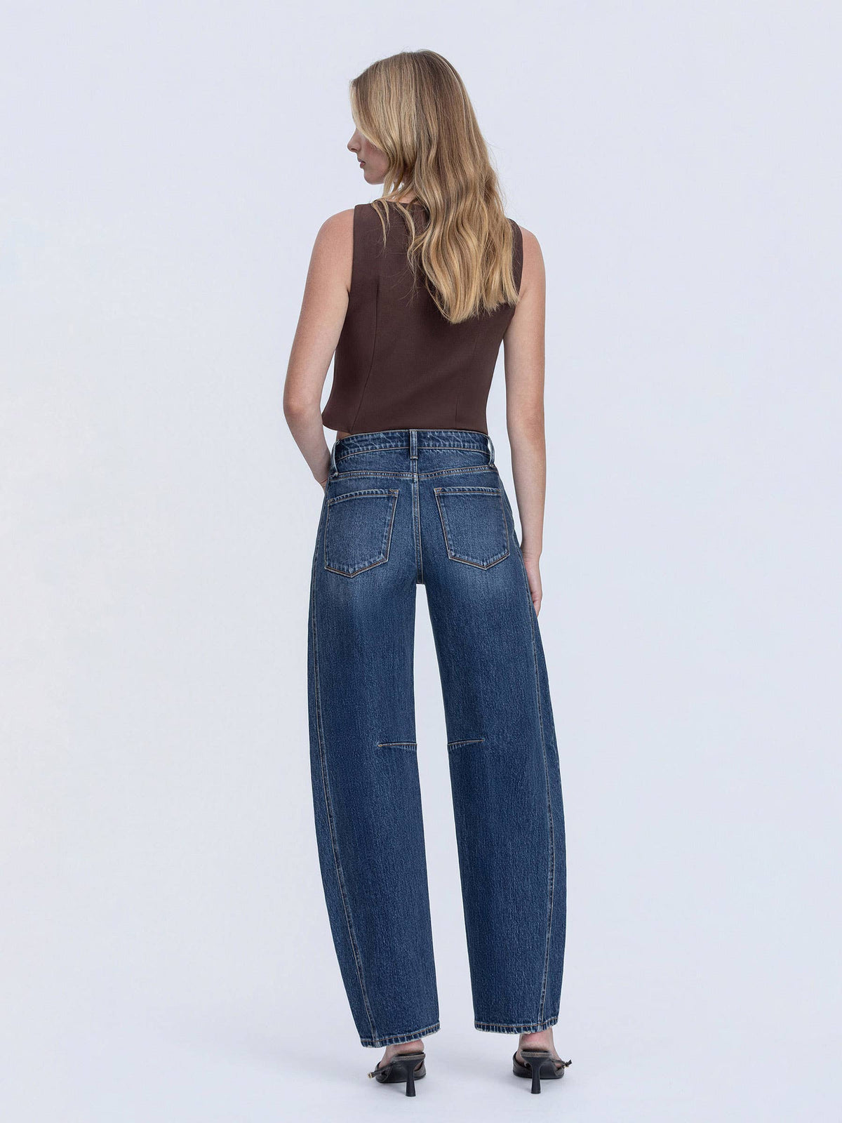 Woman wearing blue jeans and a brown top on a white background