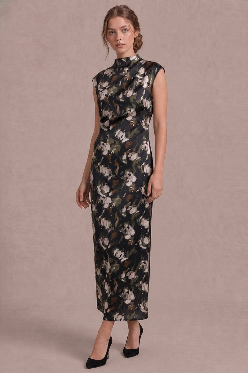 A woman modeling a sleeveless, high-neck midi dress with a dark floral print, standing against a solid mauve-pink studio background.