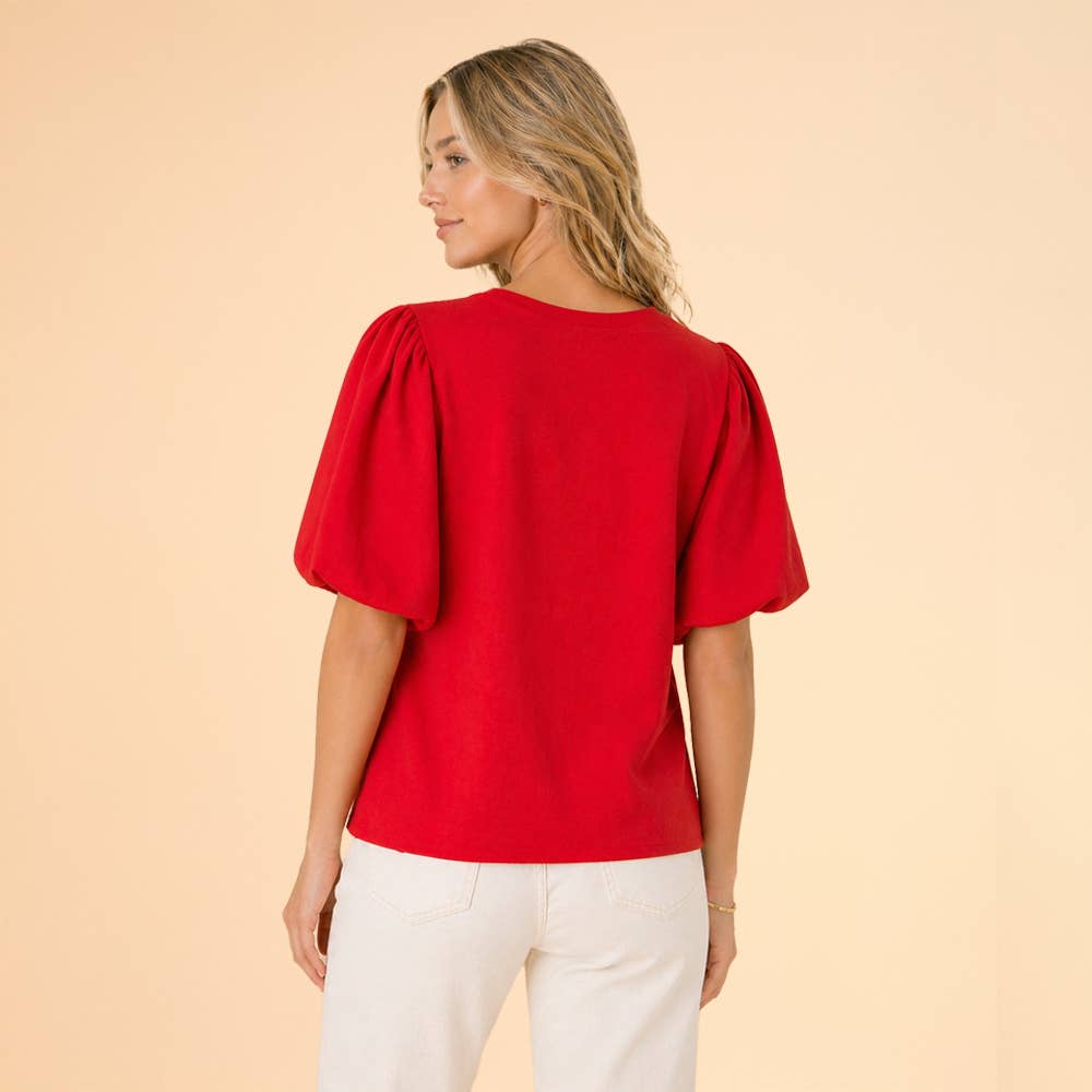Woman wearing a red blouse with puff sleeves on a beige background