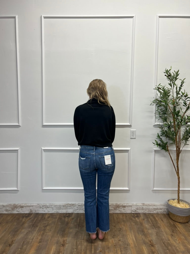 Person wearing blue jeans and a black top standing in front of a white paneled wall.