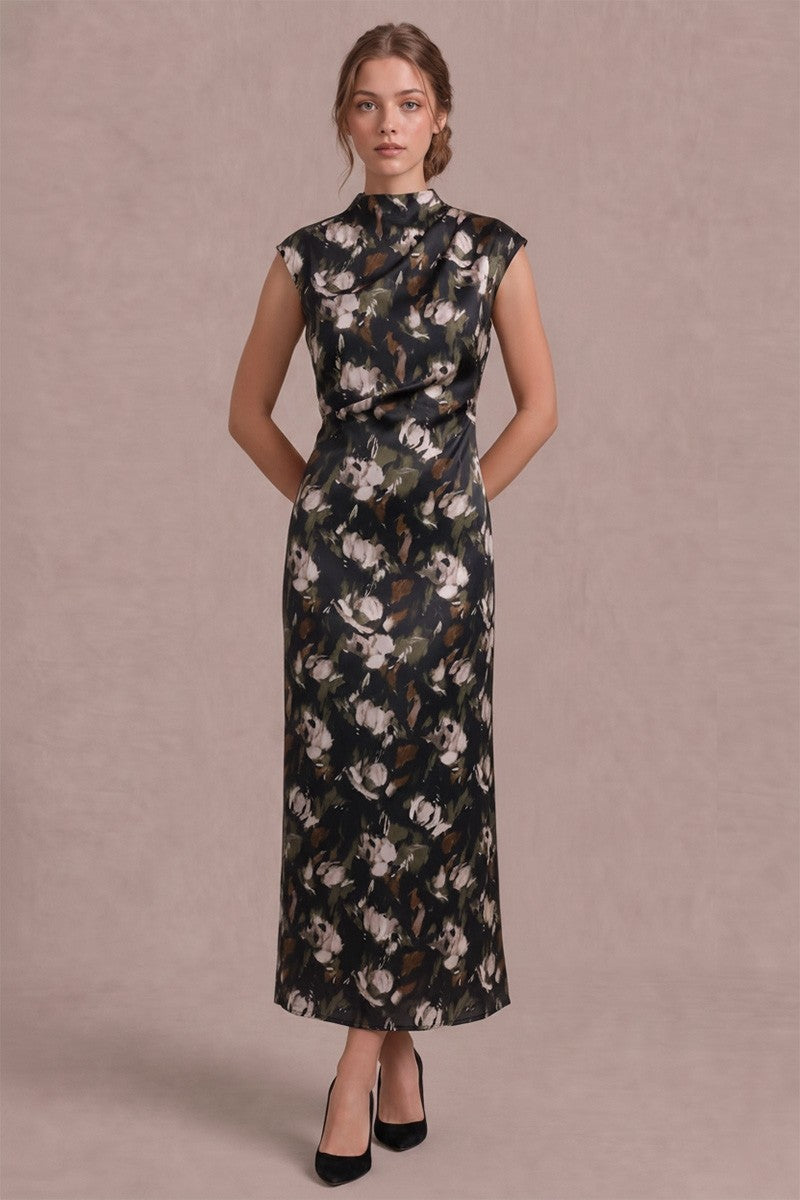 A woman modeling a sleeveless, high-neck, floor-length dress with a dark floral print, standing against a solid mauve-pink studio backdrop.