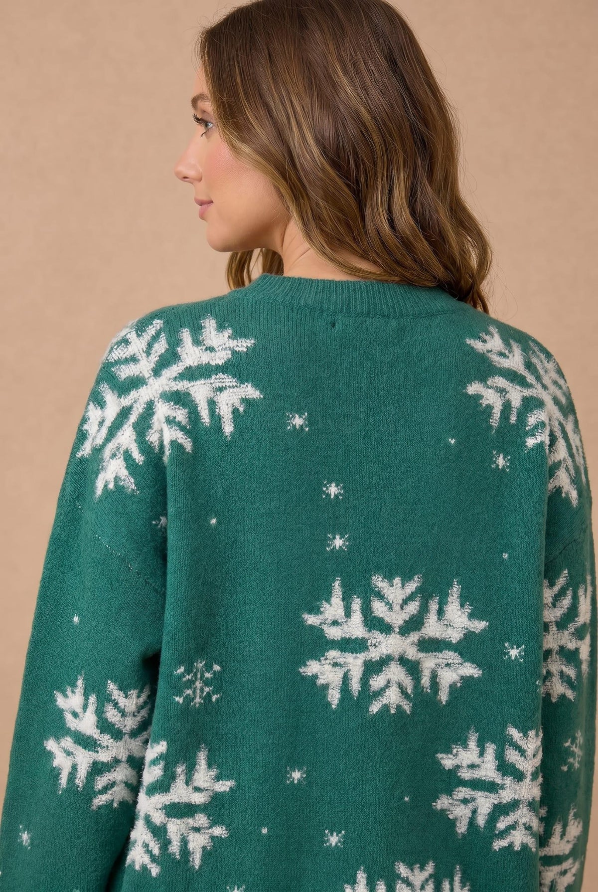 A woman wearing a green knit sweater with a white snowflake pattern, shown from the back against a plain beige background.