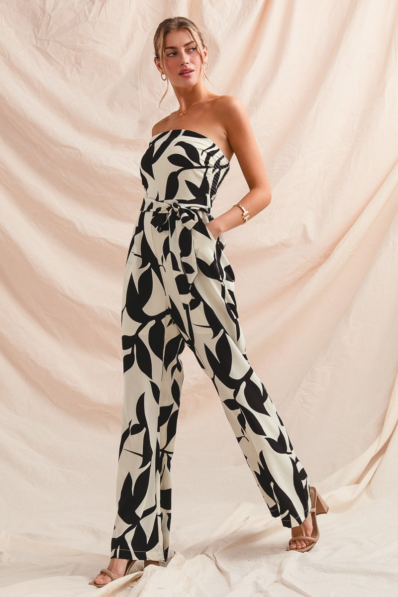 Woman wearing a strapless black and white leaf-patterned jumpsuit against a beige backdrop