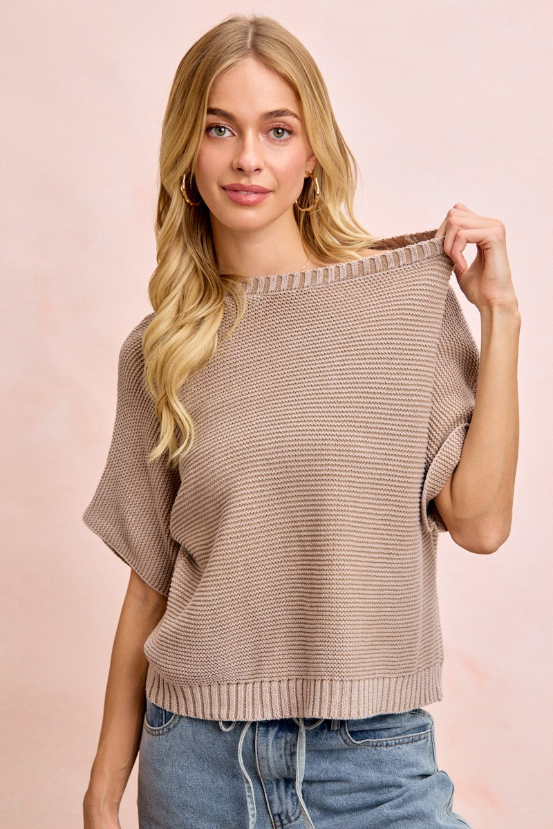 Woman wearing a beige sweater and blue jeans against a pink background