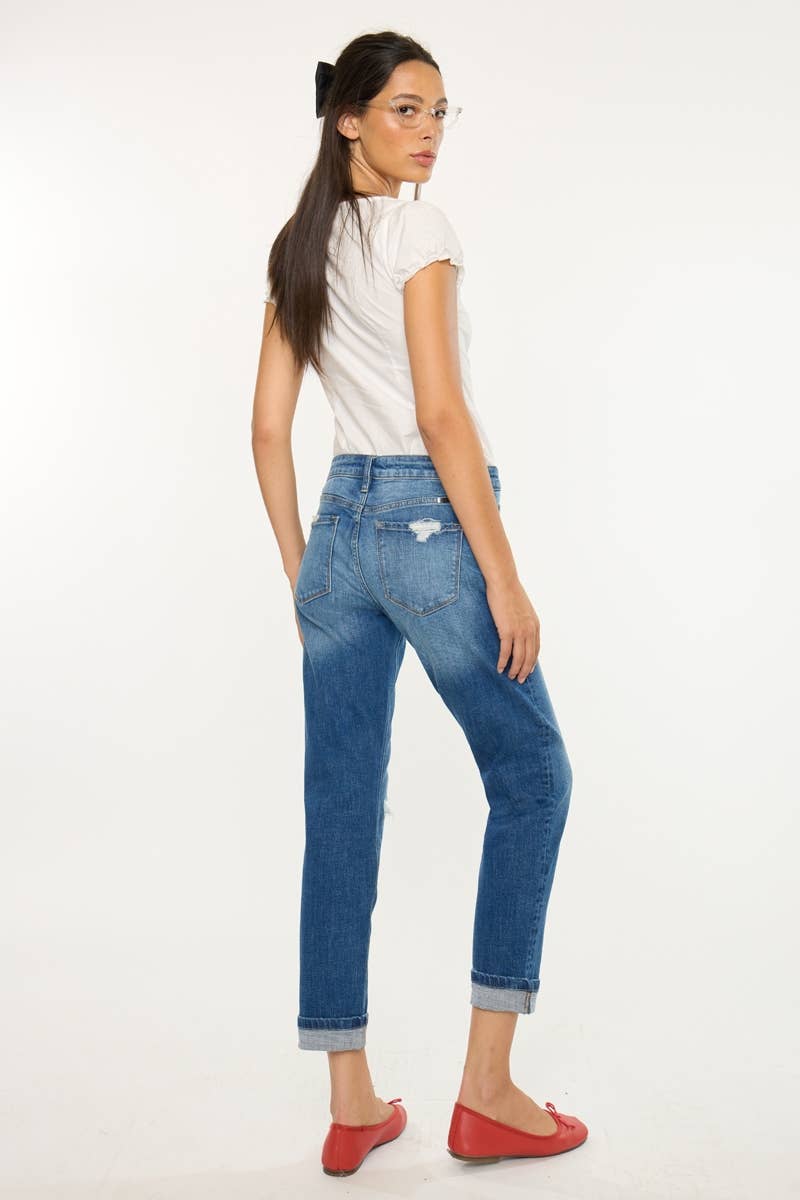 A woman shown from the back wearing blue cuffed jeans, a white short-sleeve top, and red flats against a plain white studio background.