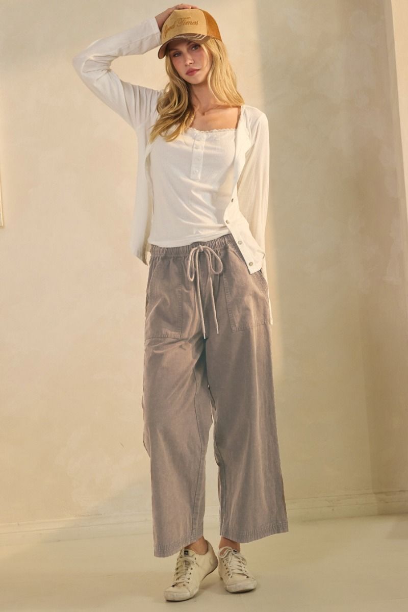 Woman wearing a white top, beige pants, and a beige cap against a plain background
