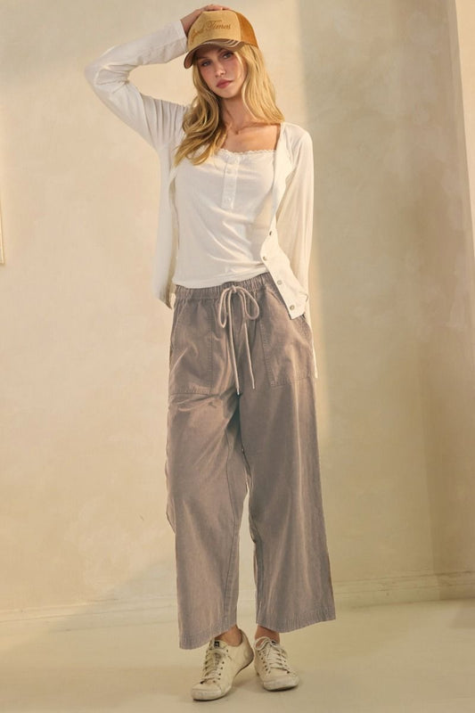 Woman wearing a white top, beige pants, and a beige cap against a plain background