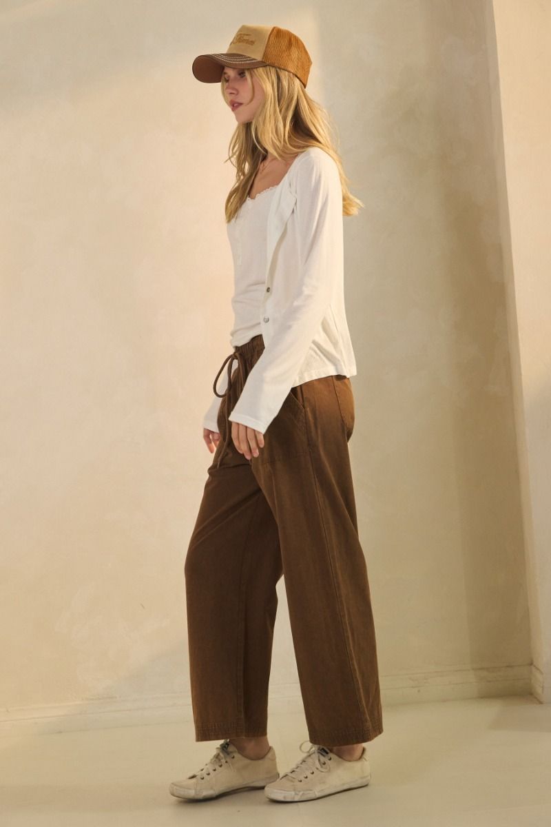 Woman wearing a white top, brown pants, and a beige cap against a plain background