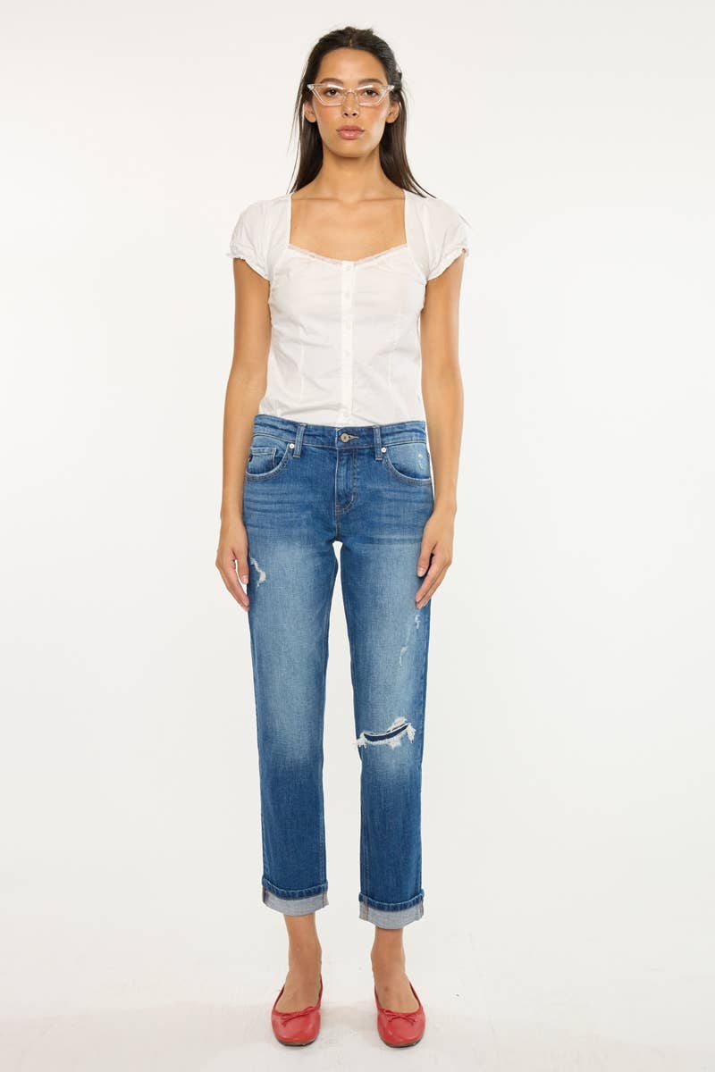 A woman modeling a white short-sleeve top and distressed blue cropped jeans with rolled hems, paired with red shoes, against a plain white studio background.