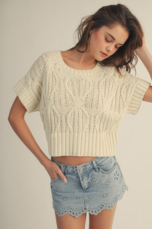 Woman wearing a beige knitted top and denim shorts on a plain background
