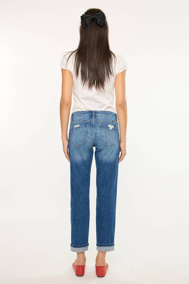 A woman viewed from behind wearing blue denim jeans with a faded wash, a white t-shirt, and red shoes against a plain white background.