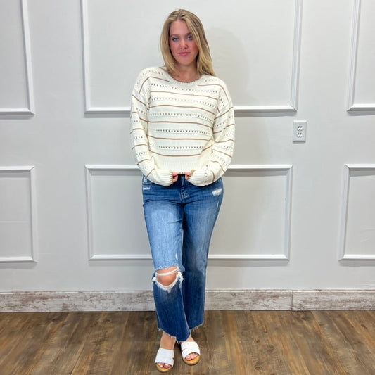 Woman wearing a striped sweater and jeans standing in a room with white paneled walls.
