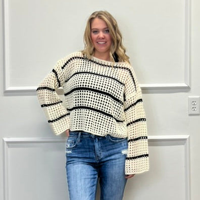Woman wearing a striped sweater and jeans standing in a room with a white wall and wooden floor.
