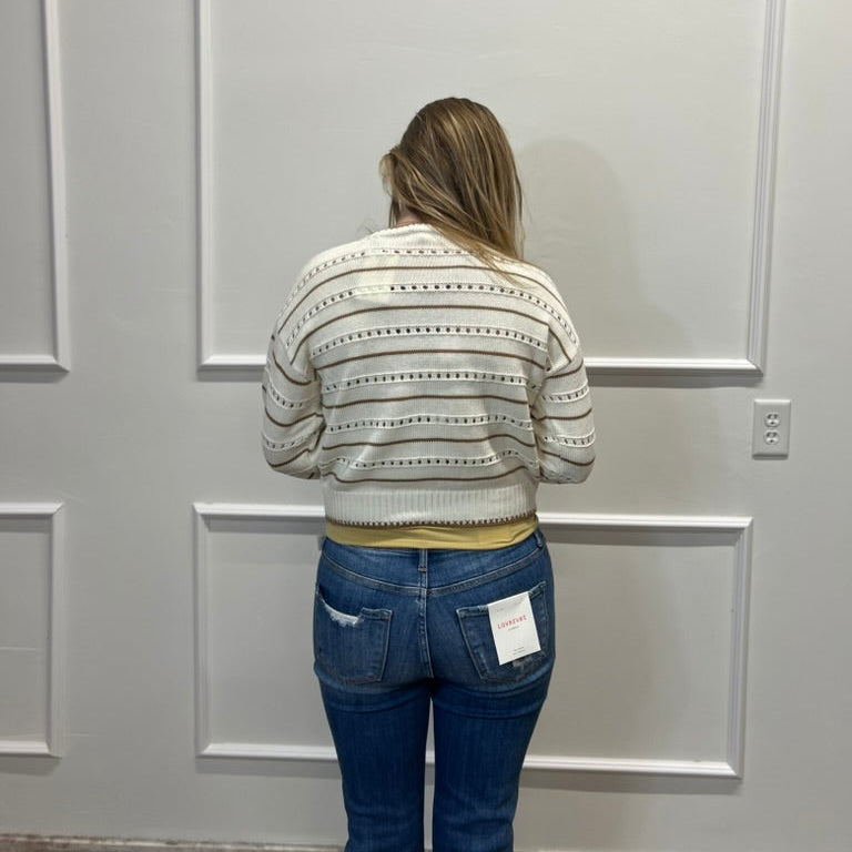 Person wearing a patterned sweater and blue jeans standing against a gray paneled wall.
