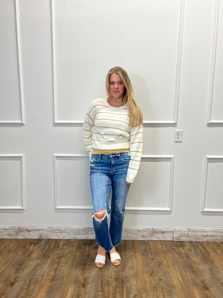 Woman wearing a striped sweater and jeans standing against a white paneled wall.