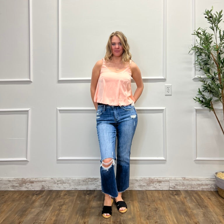 Woman wearing a pink top and blue jeans standing against a white paneled wall.