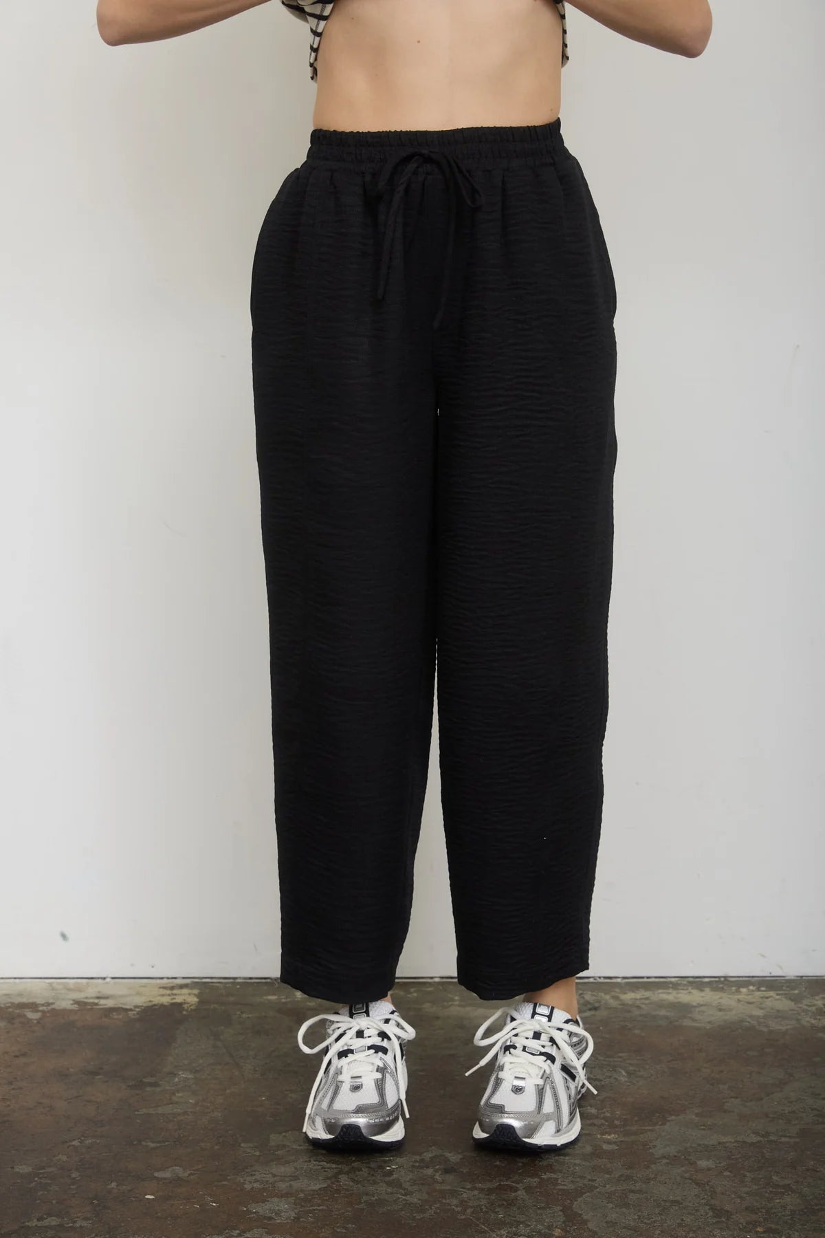 Person wearing black high-waisted pants and silver sneakers on a plain background