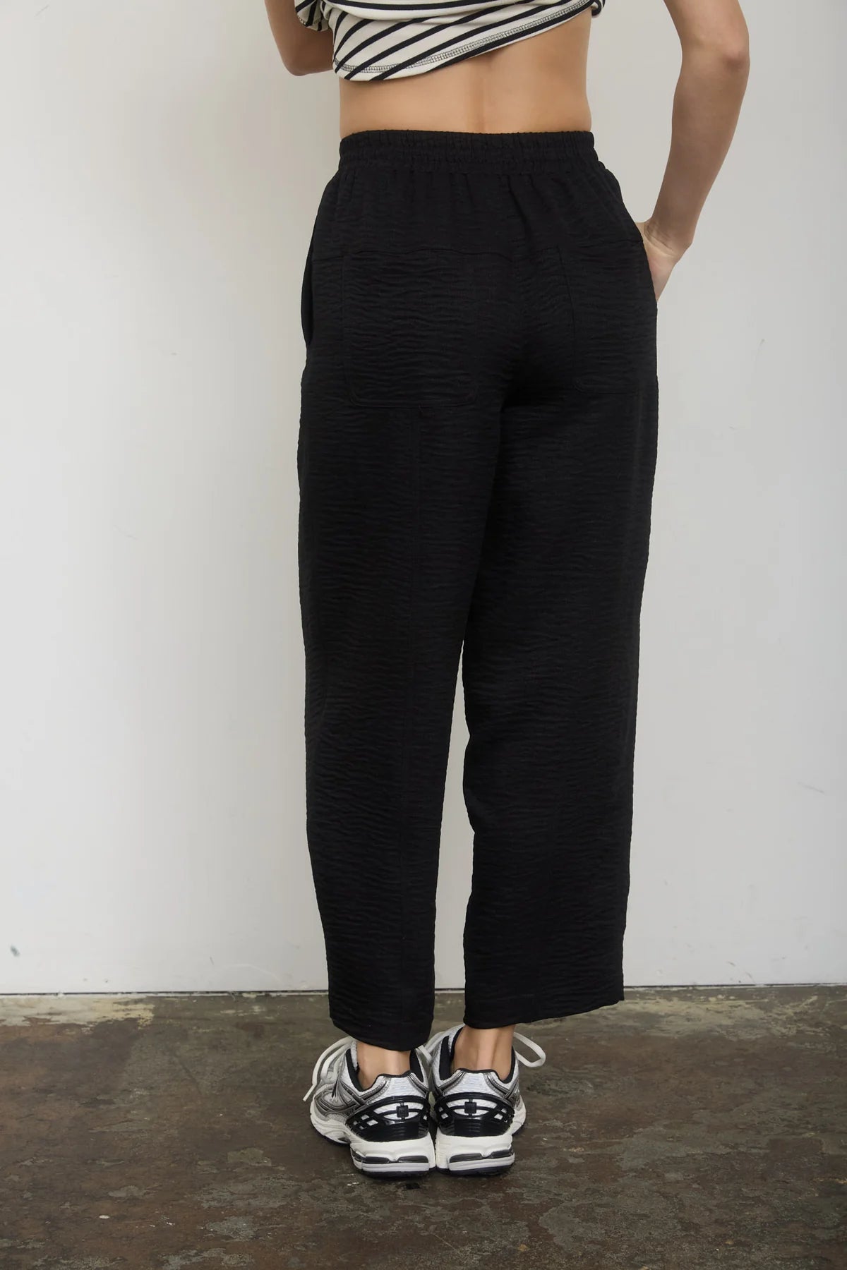 Person wearing black high-waisted pants and black and white sneakers on a plain background