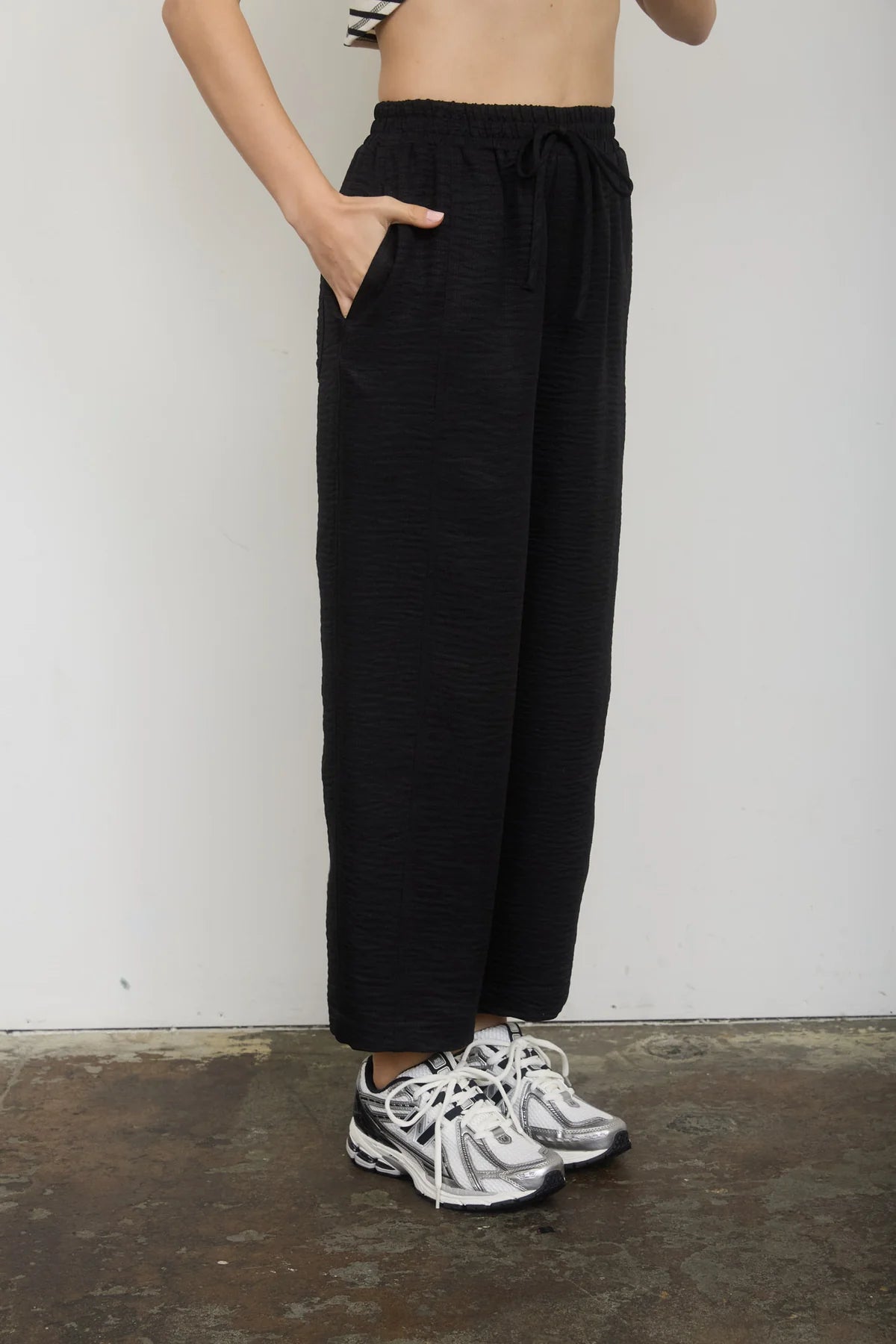 Person wearing black pants and white sneakers against a plain background