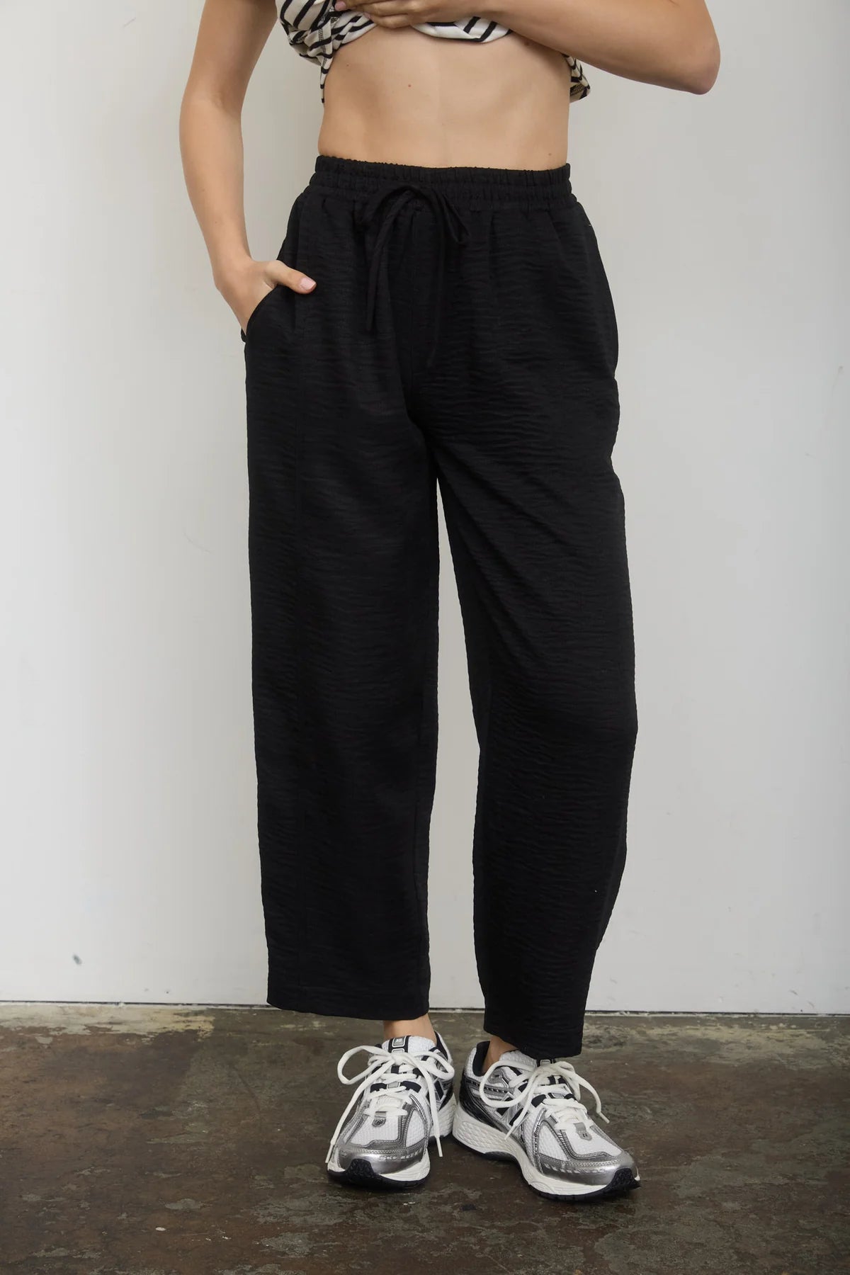 Person wearing black pants and gray sneakers against a plain background