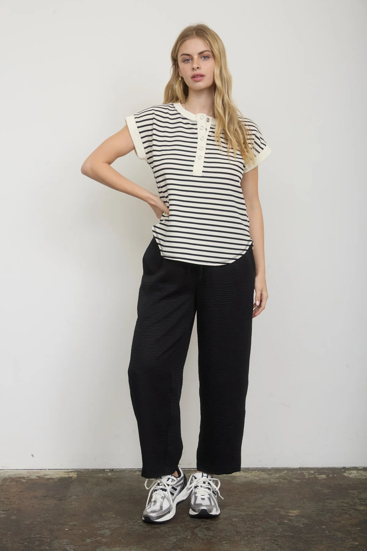Woman wearing a striped shirt and black pants against a white wall