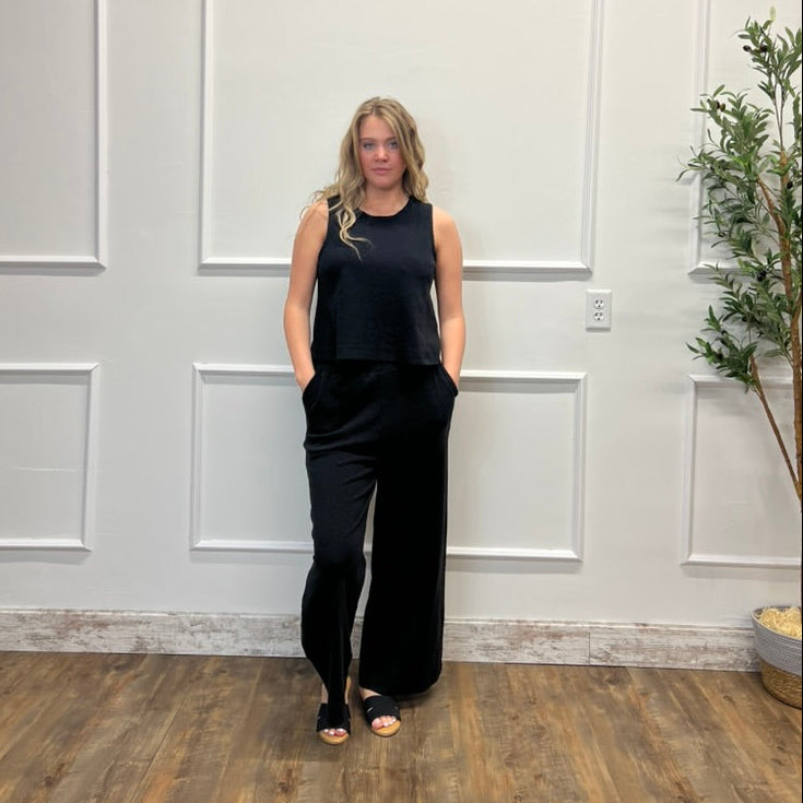 Woman in a black outfit standing against a white paneled wall.