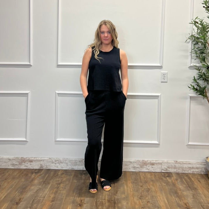 Woman in a black outfit standing against a white paneled wall.