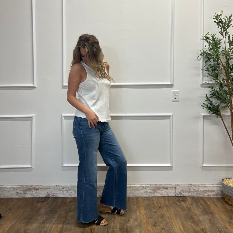 Woman in a white top and blue jeans standing in a room with white paneled walls and a plant.