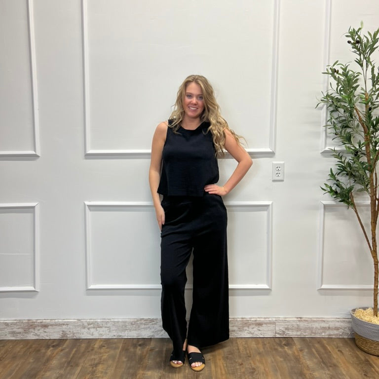Woman in a black outfit standing in a room with white paneled walls and a plant.