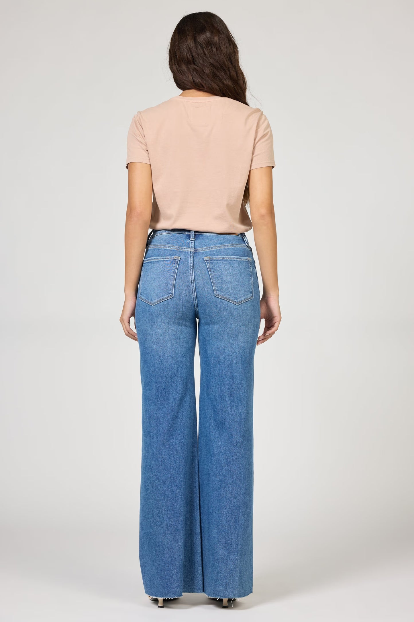 Woman wearing a beige top and blue jeans on a white background