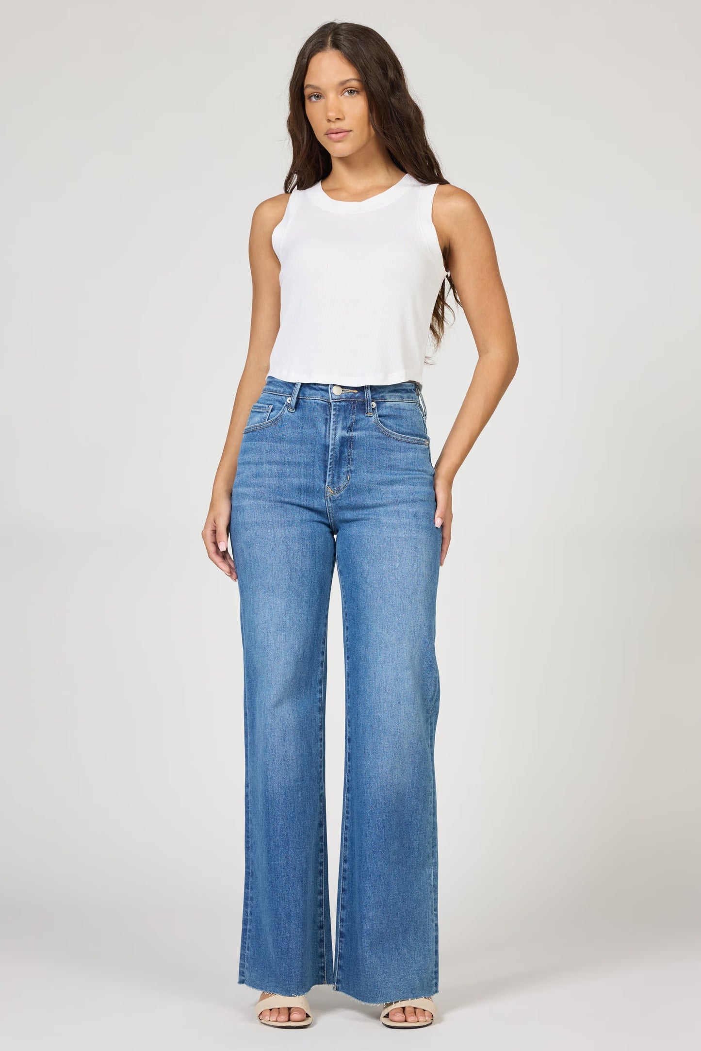 Woman wearing a white sleeveless top and blue jeans on a white background