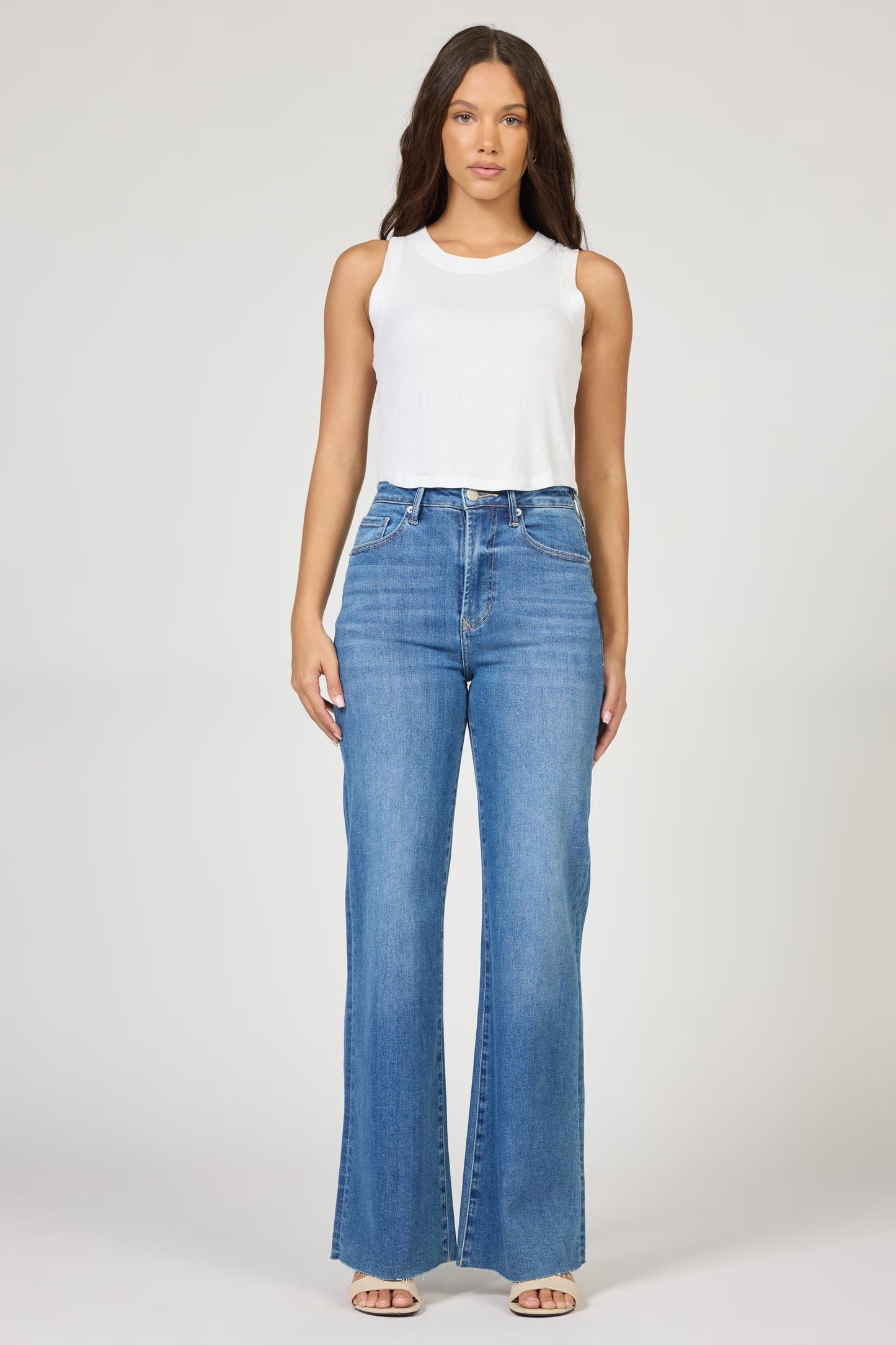 Woman wearing a white sleeveless top and blue jeans on a white background