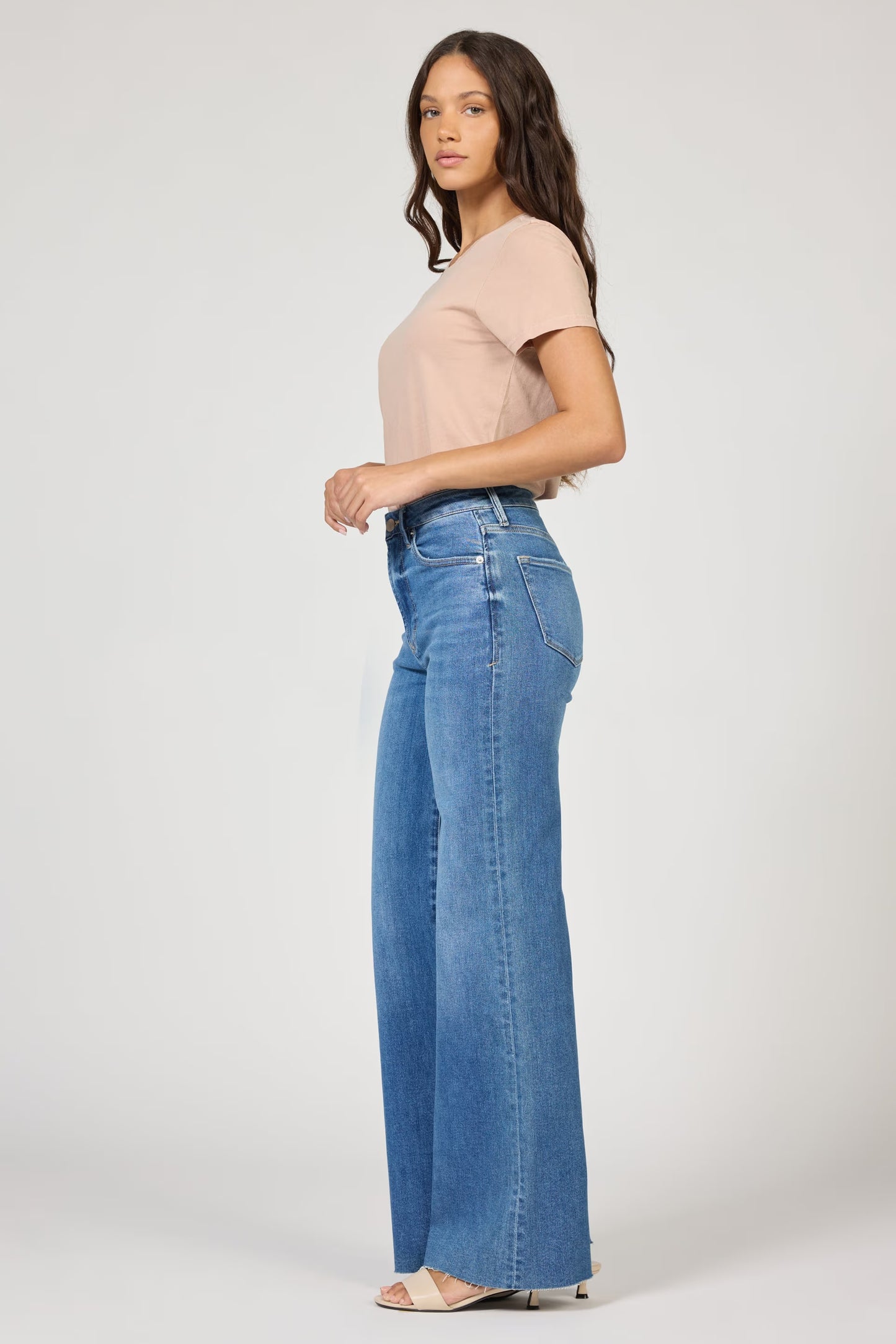 Woman wearing a beige top and blue jeans on a white background