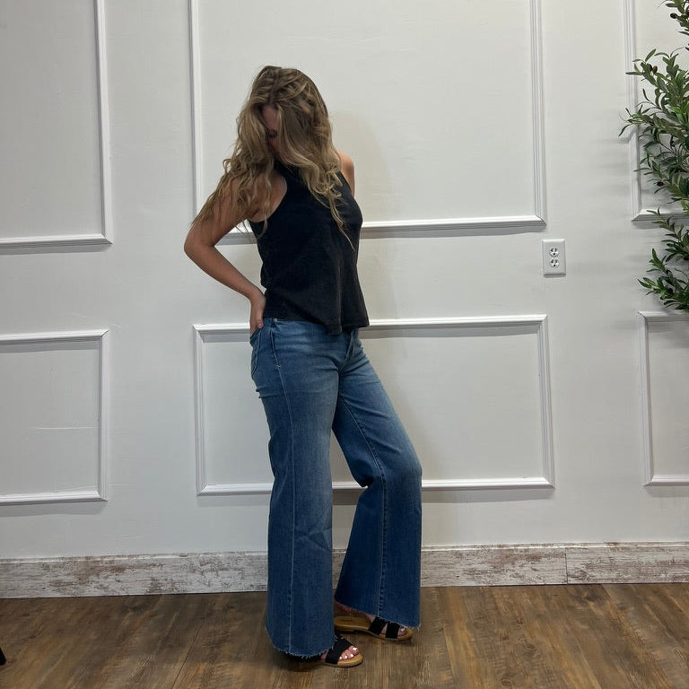 Woman wearing a black top and blue jeans standing against a white paneled wall.