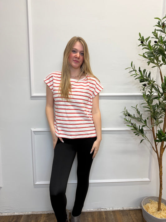 Woman wearing a red and white striped shirt and black pants standing in front of a white door.