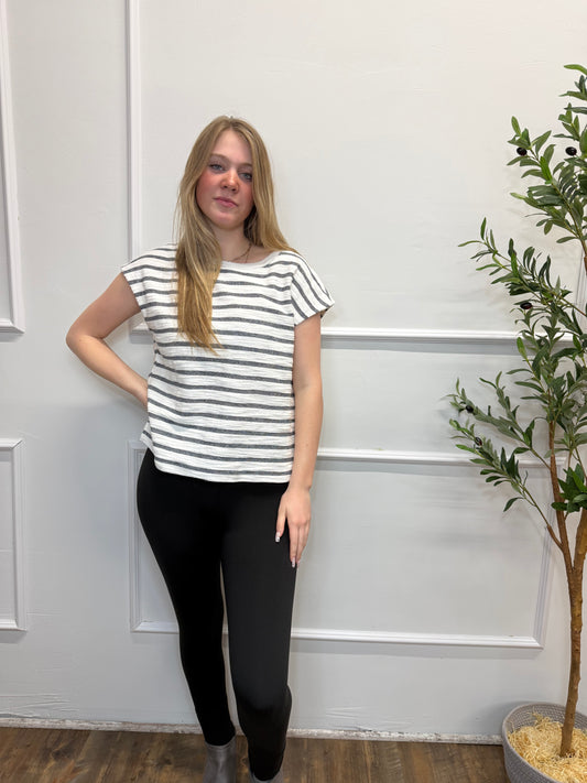 Woman wearing a striped shirt and black pants standing in front of a white door with a plant above.