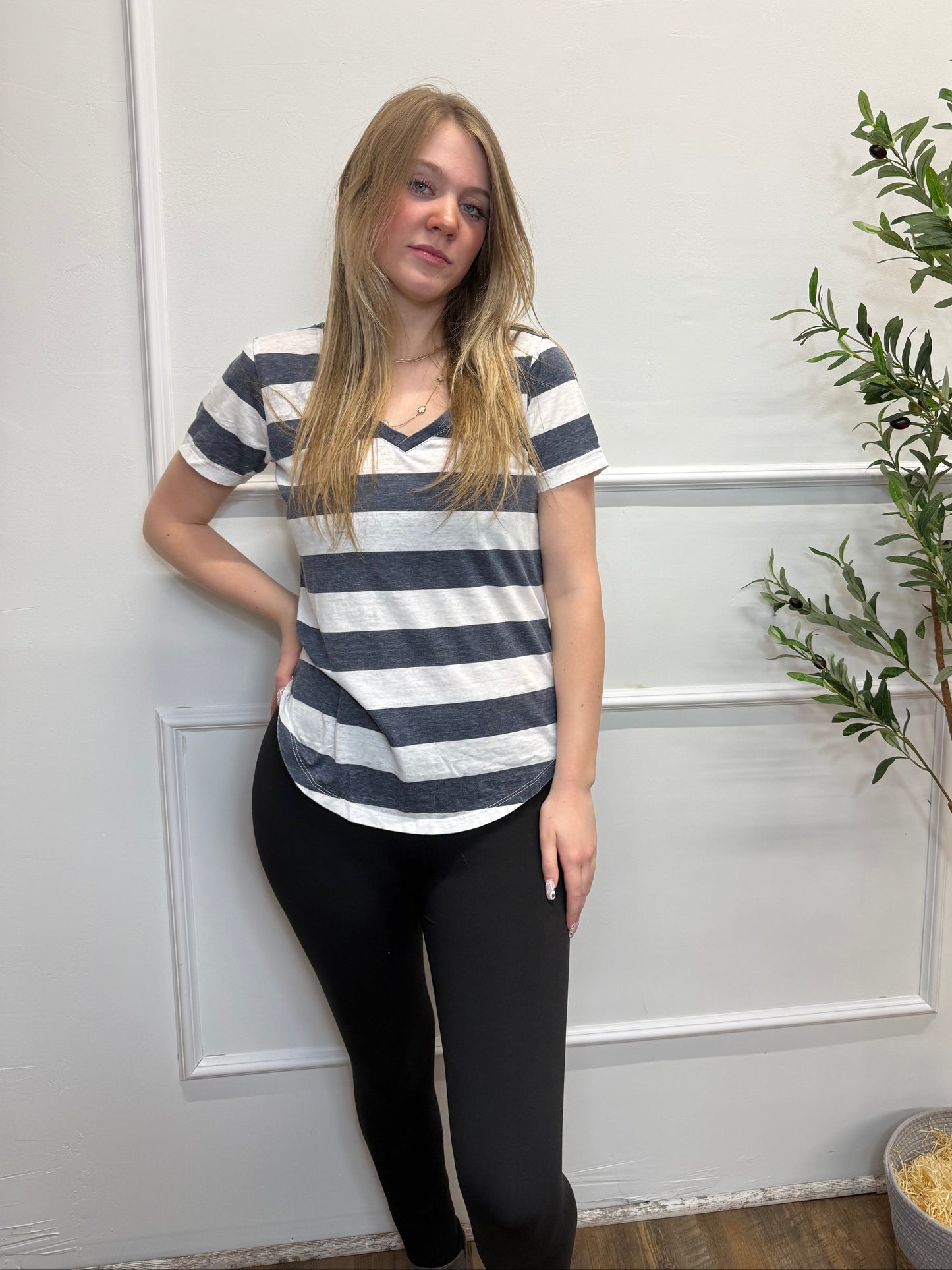 Person wearing a striped shirt and black pants standing in front of a white door with greenery.